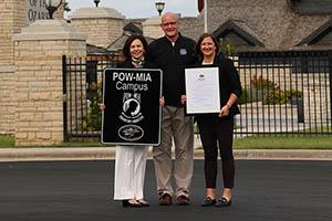 Man and two women standing in front of iron fence and brick pillars.