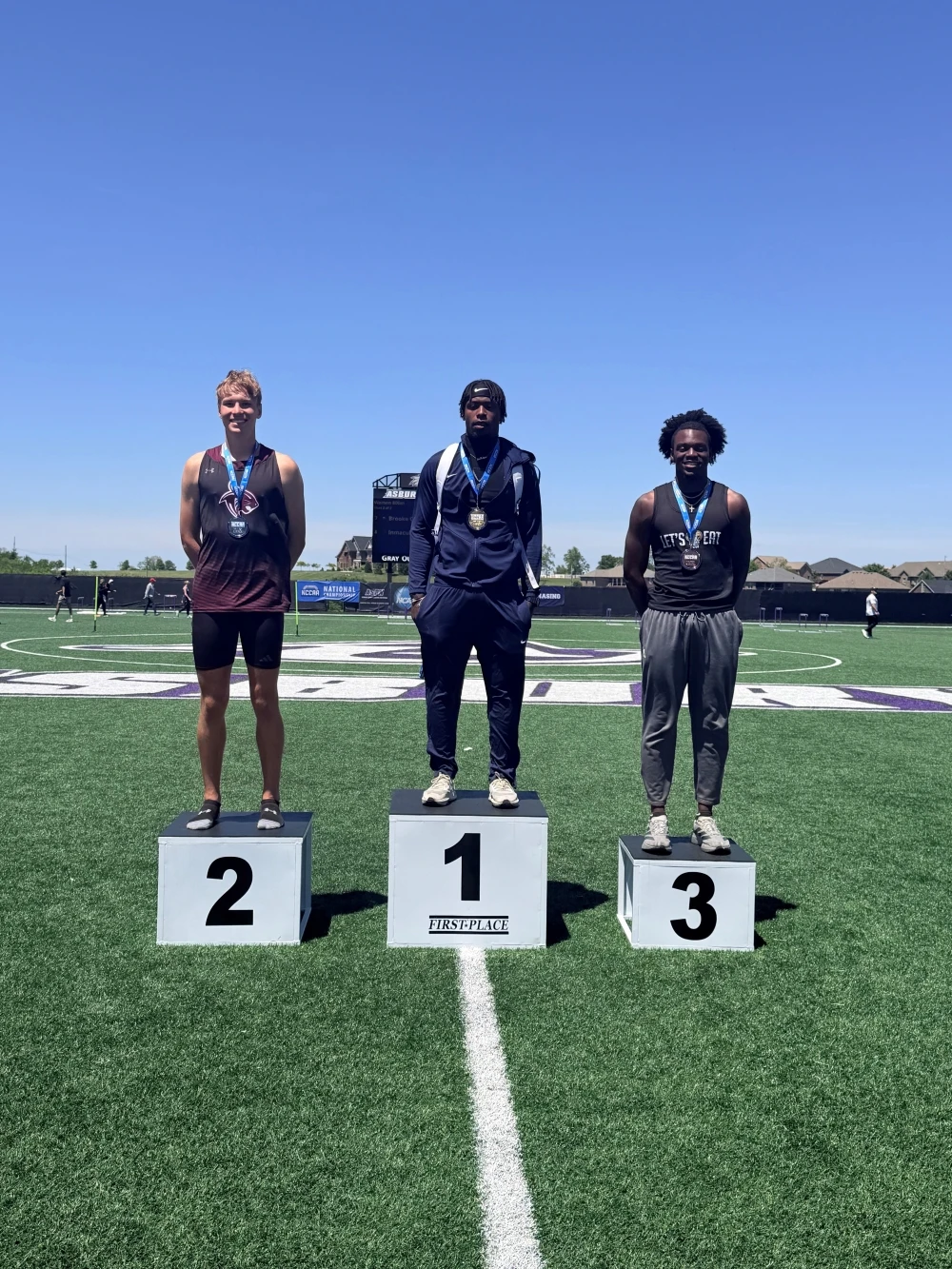 This image depicts three men standing on podiums ranked from 3rd place to 1st. They are wearing track uniforms. 