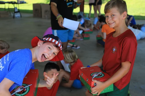 Two children smiling while holding a "Operation Christmas Child" box. 