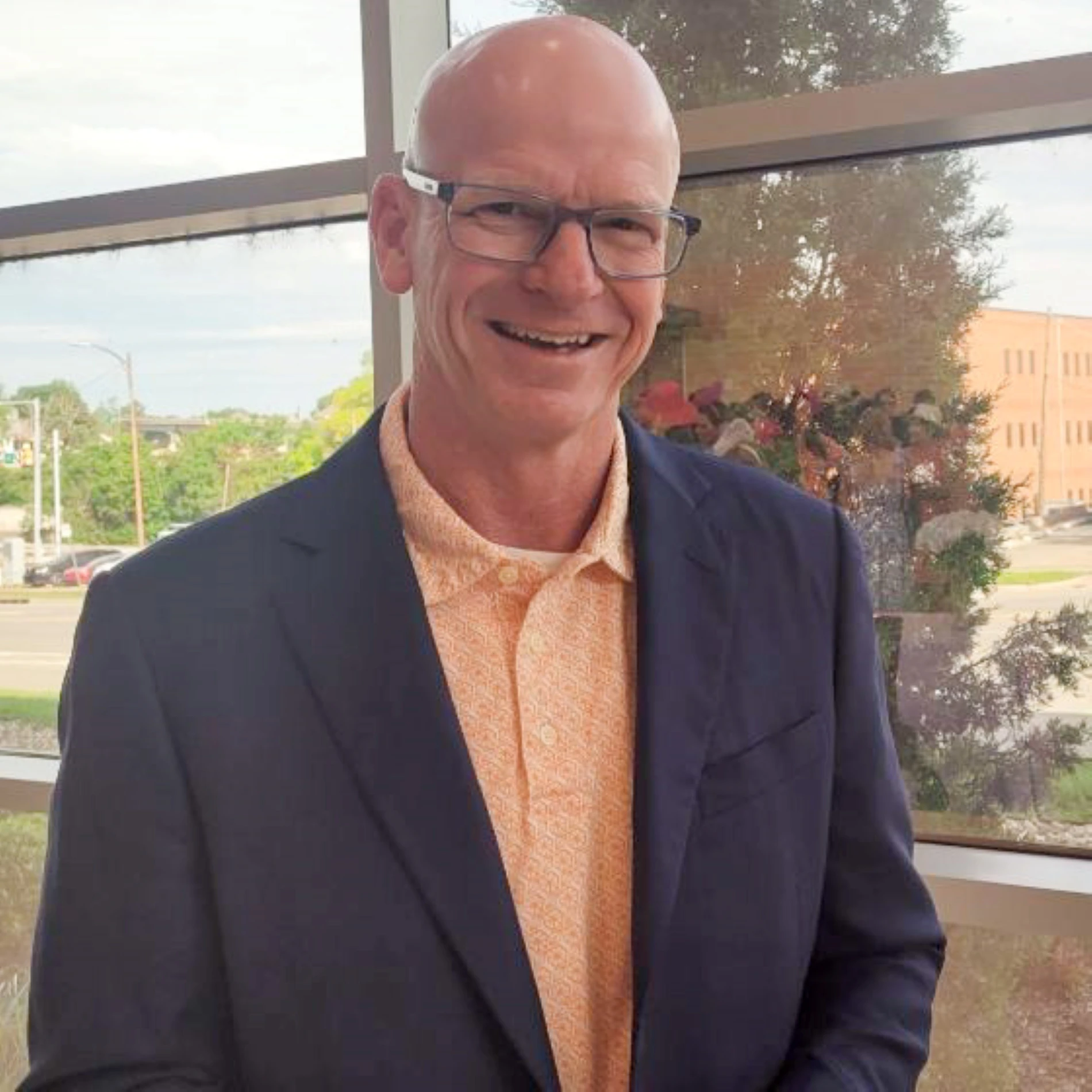 This image depicts a man smiling in front of a grew background. 