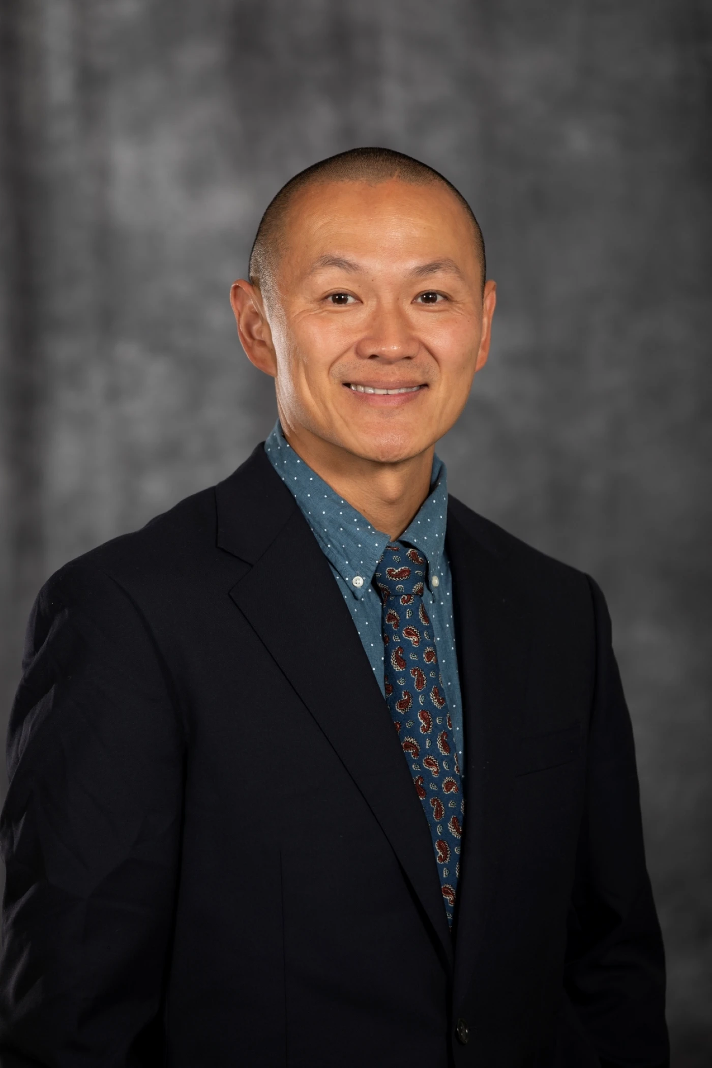 This image depicts a man smiling in front of a grew background. 