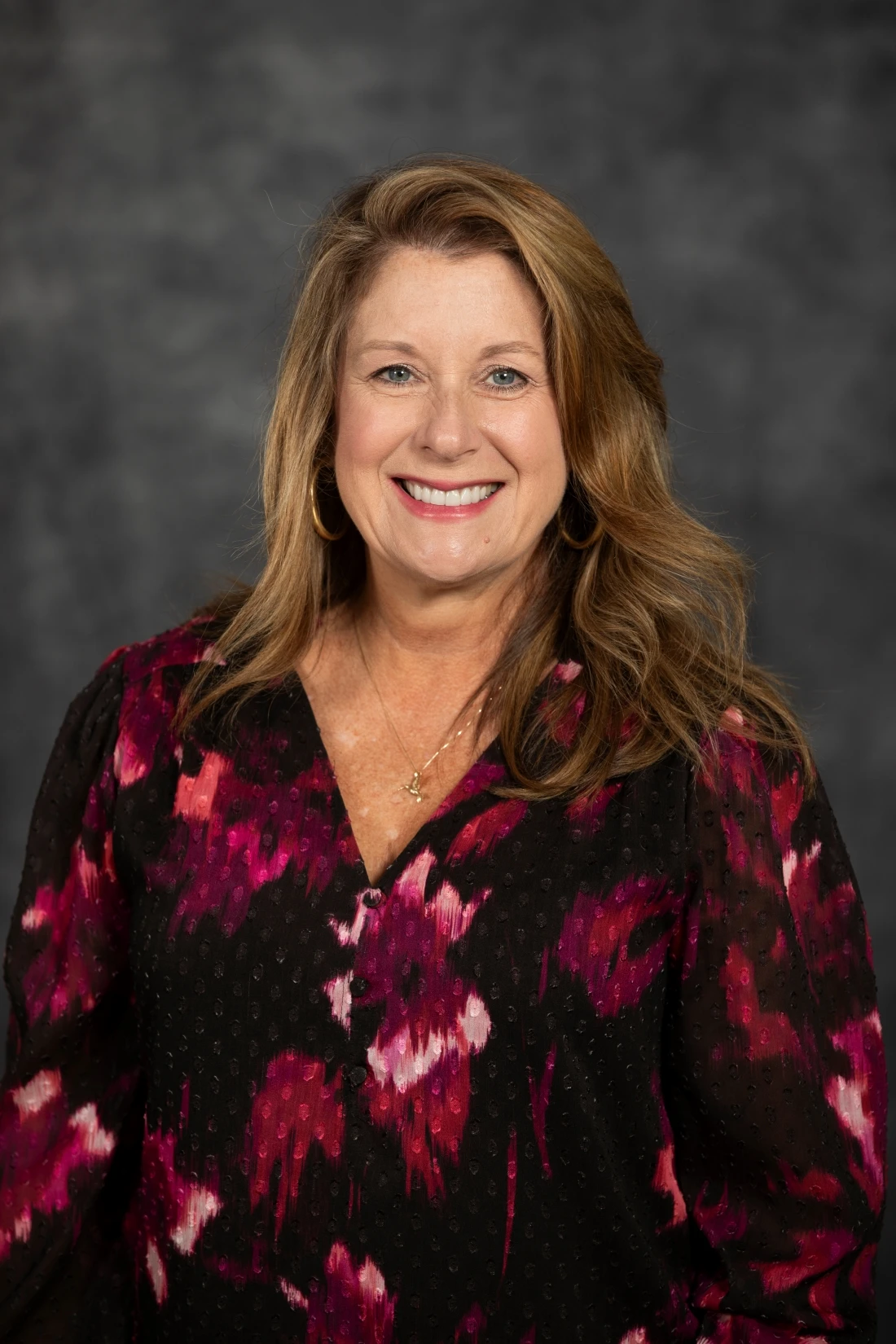 This image depicts a woman smiling in front of a grew background. 