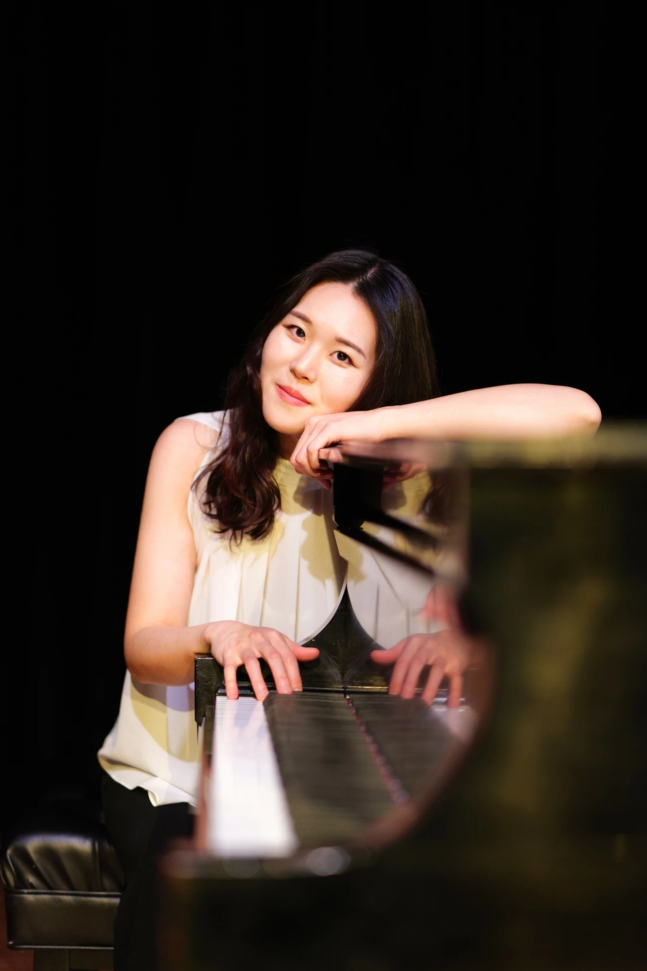 This image depicts a woman smiling behind a piano. 
