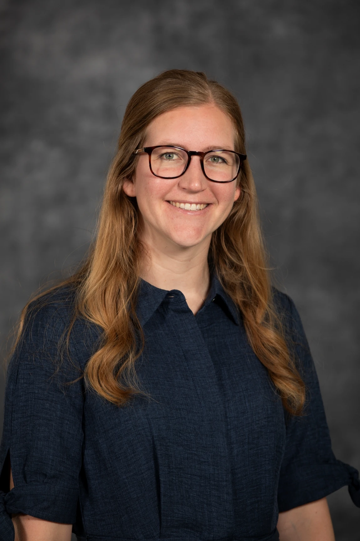 This image depicts a woman smiling in front of a grew background. 