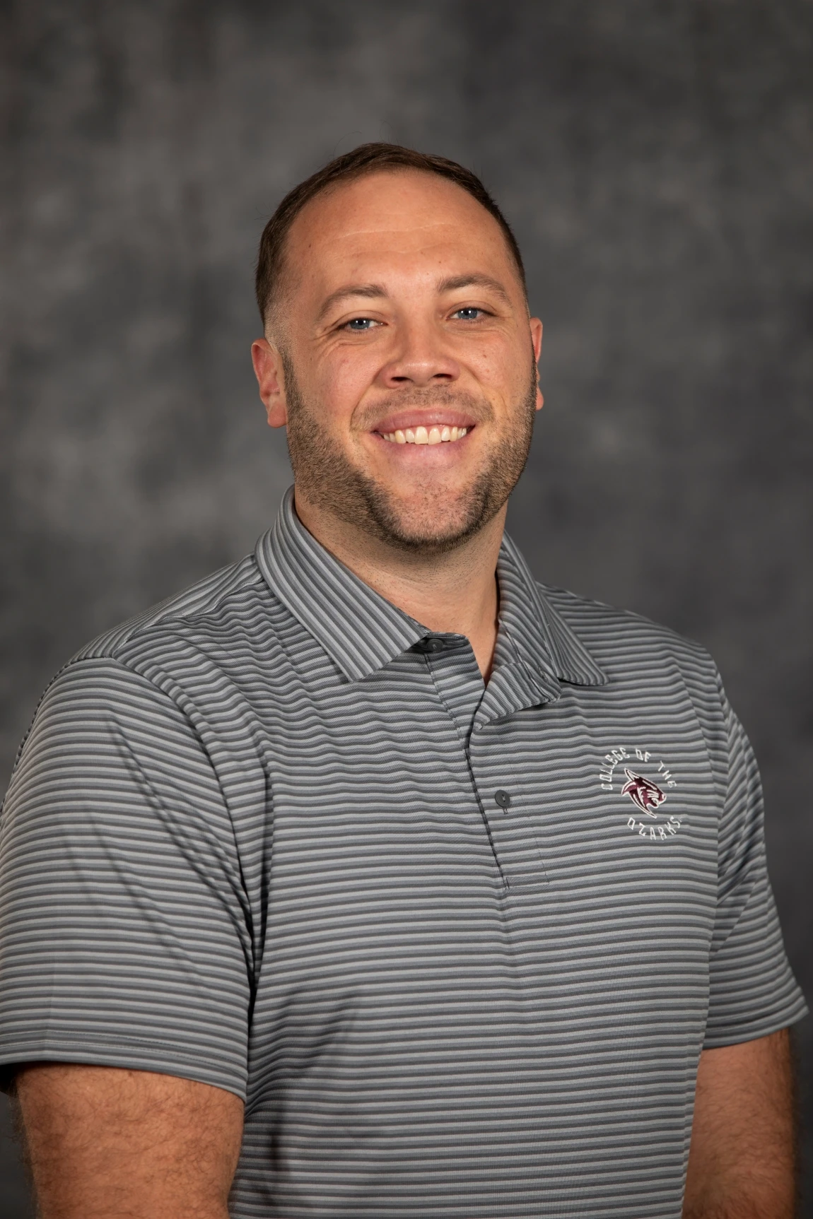 This image depicts a man smiling in front of a grew background. 