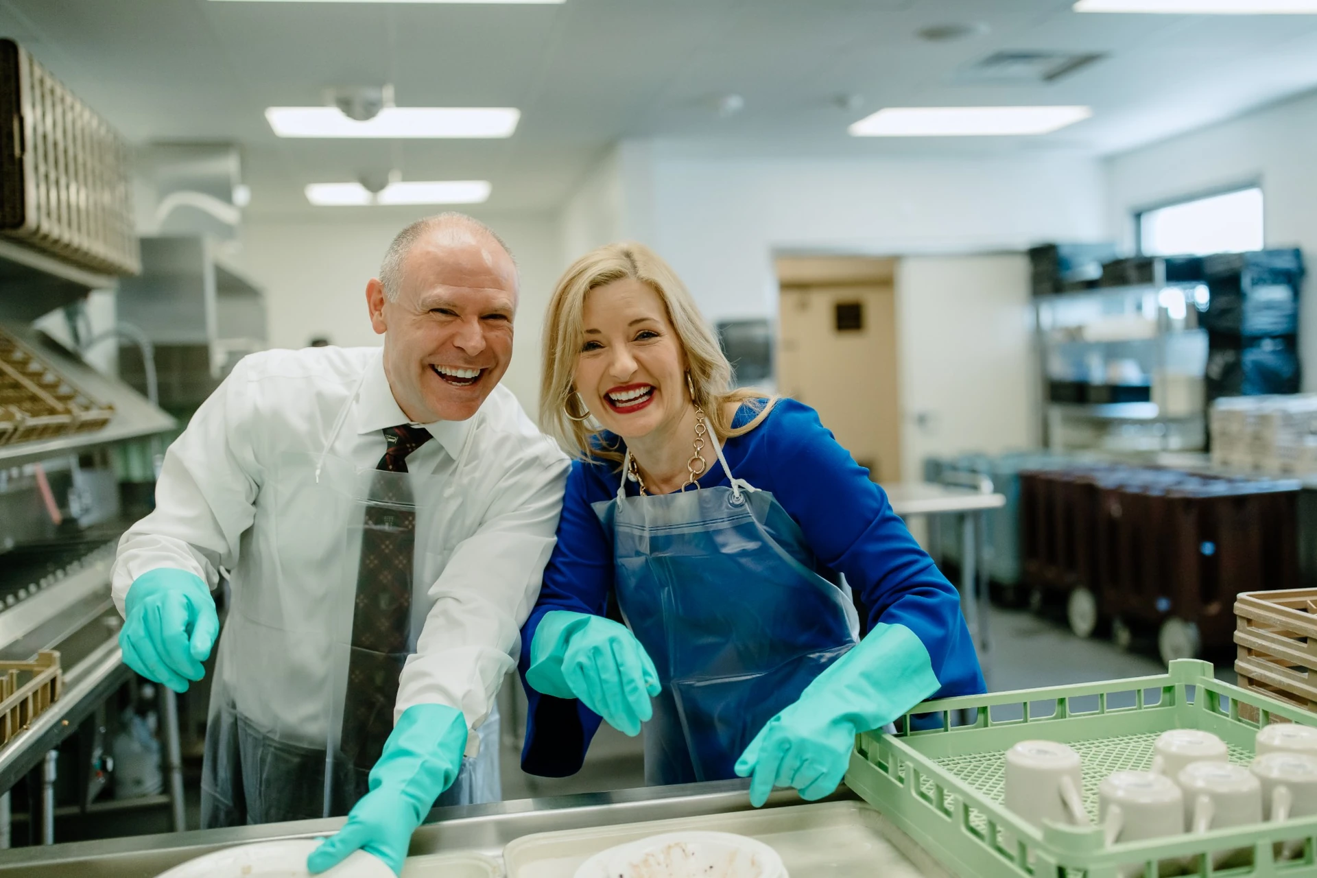 President Brad Johnson and First Lady Laura Johnson laughing while washing dishes in a campus kitchen