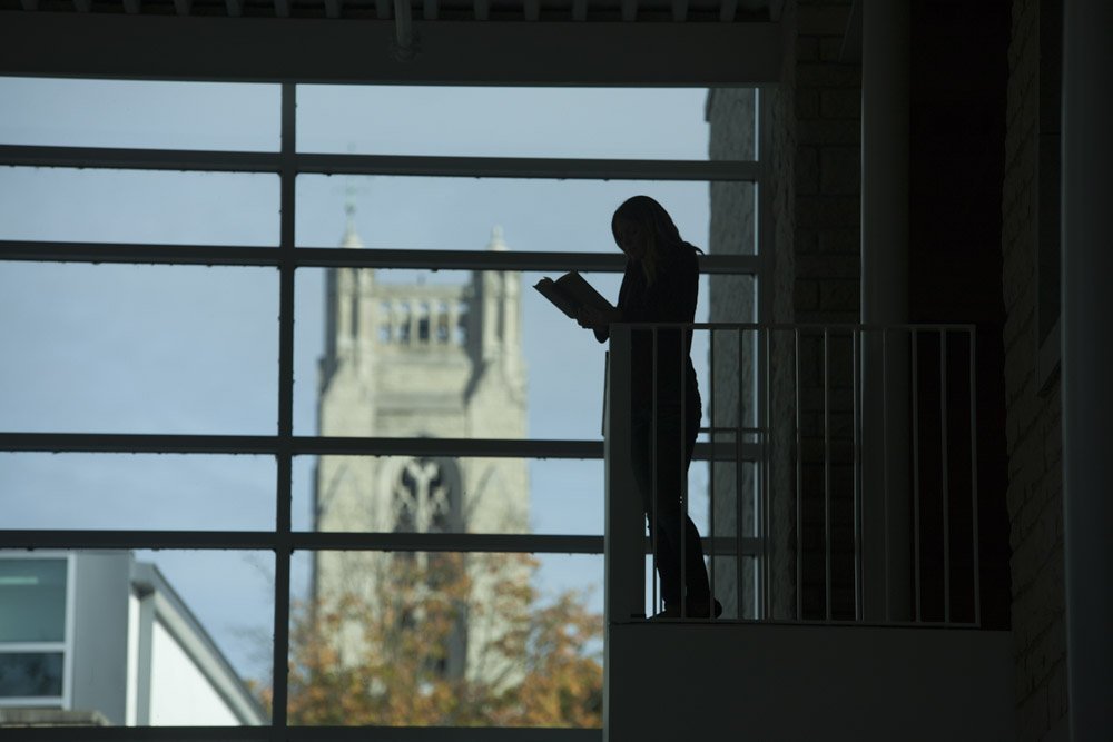 Student reading her bible in a relatively dark place with the chapel in the background