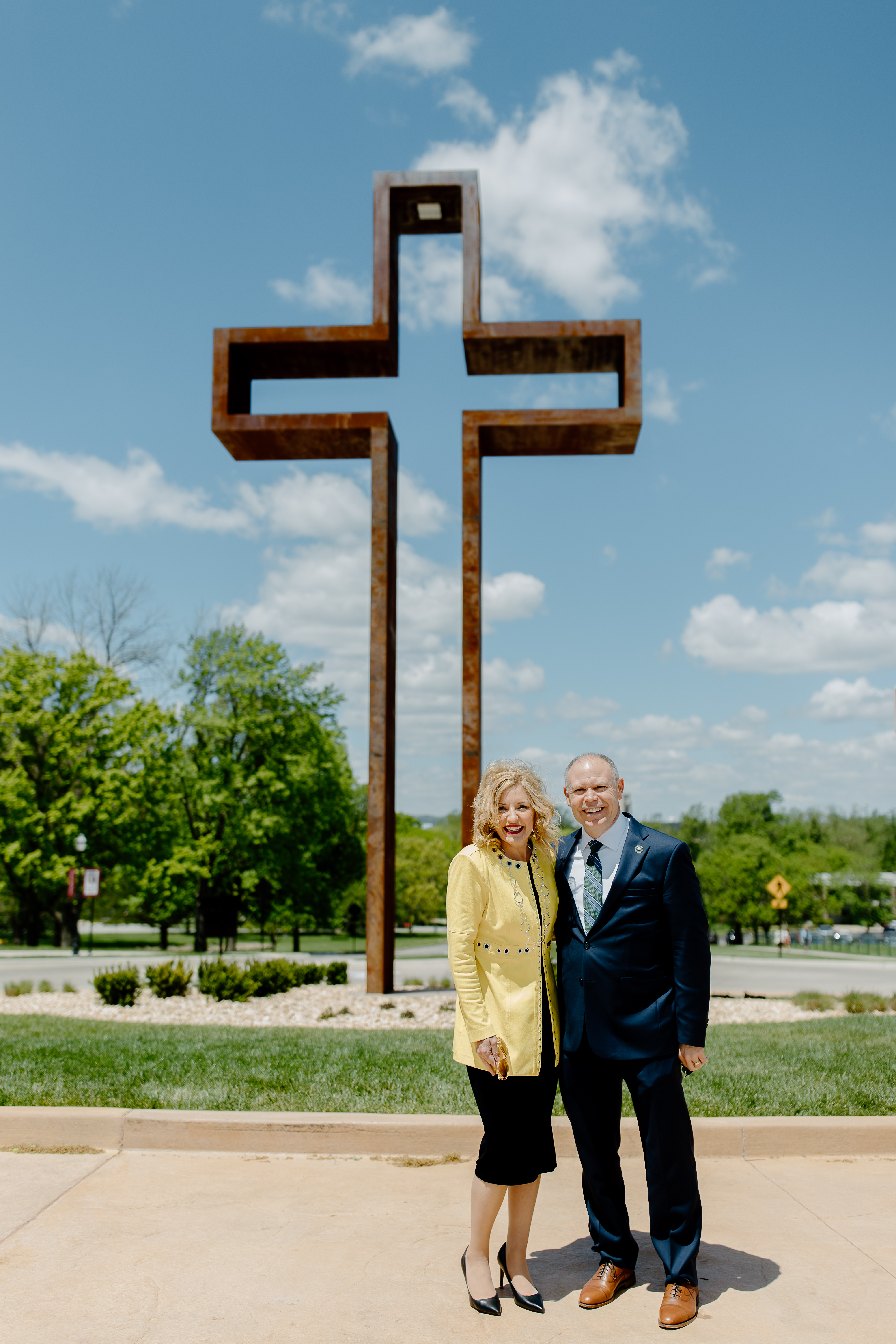 A man and woman stand in front of an cross statue