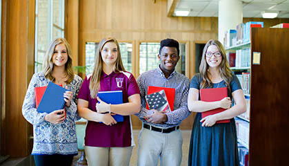 Four students holding notebooks and textbooks.