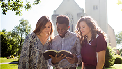 Three students reading bible in front of the chapel.