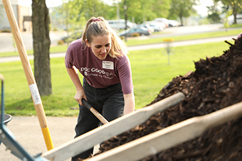 Alumna Abigail Rowe shovels mulch by the College’s Fire Station on Doc Good Day. Rowe now serves as development manager at C of O. 