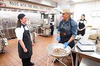 Rebekah Eatherly helps Mike Rowe make the College of the Ozarks signature fruitcake during his visit to the production kitchen. 